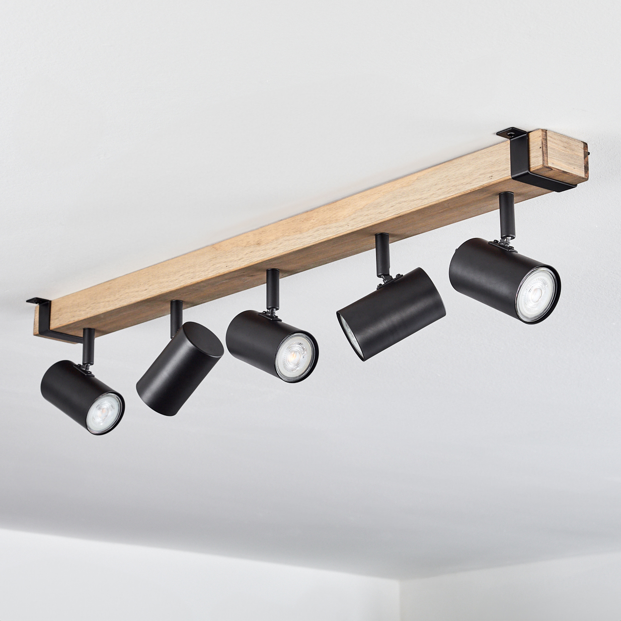 Ein Holzbalken mit fünf schwarzen Strahlern, die an einer weißen Decke befestigt sind. Die Strahler sind angewinkelt.