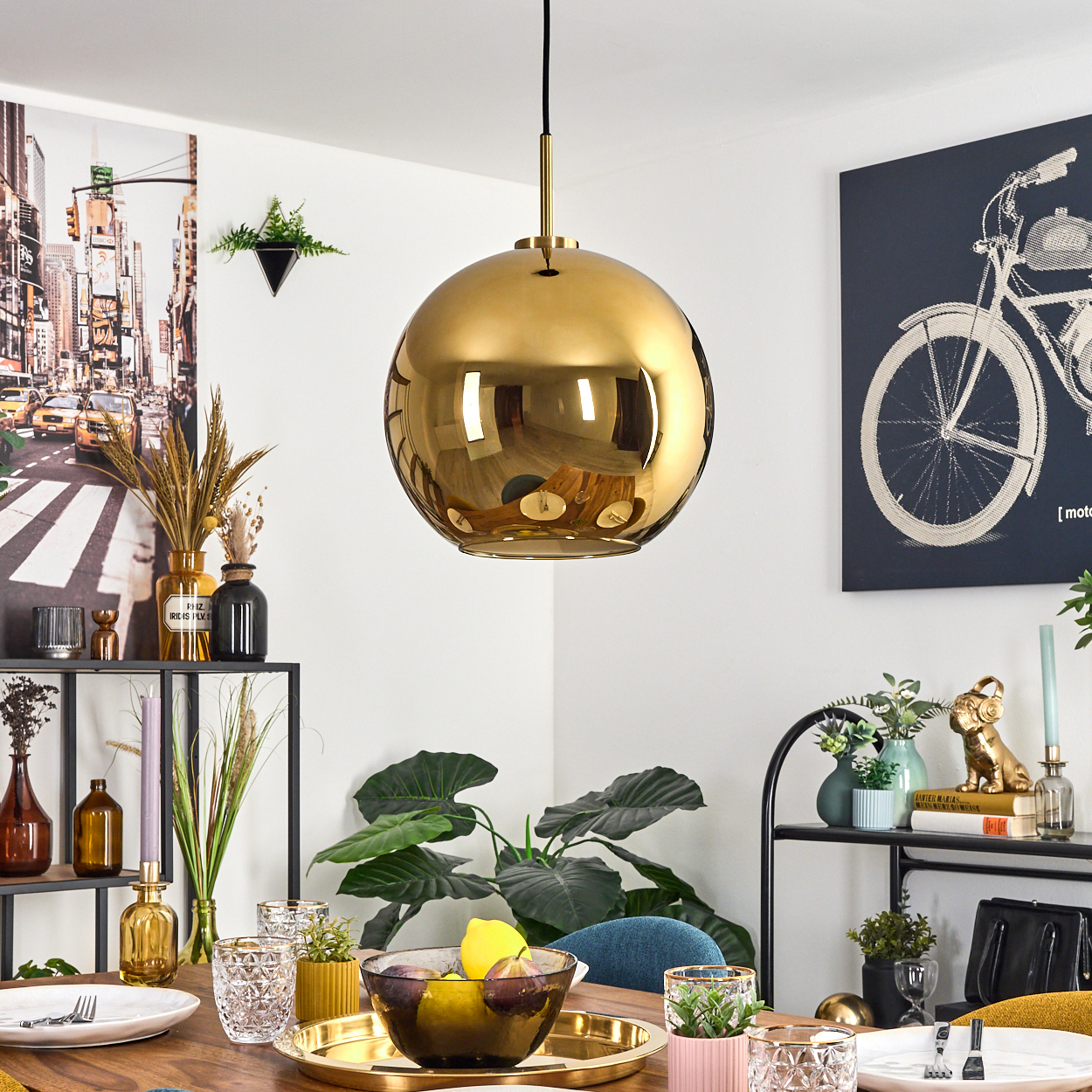 Eine goldene Kugellampe hängt über einem Tisch, der für eine Mahlzeit gedeckt ist. Der Hintergrund zeigt eine Fahrradkunst und -dekoration.