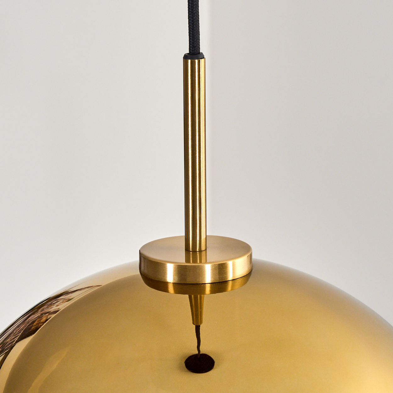 Eine goldene Pendelleuchte mit reflektierender Oberfläche hängt an einem schwarzen Kabel. Eine Messingstange und ein kreisförmiger Sockel vervollständigen das Design.