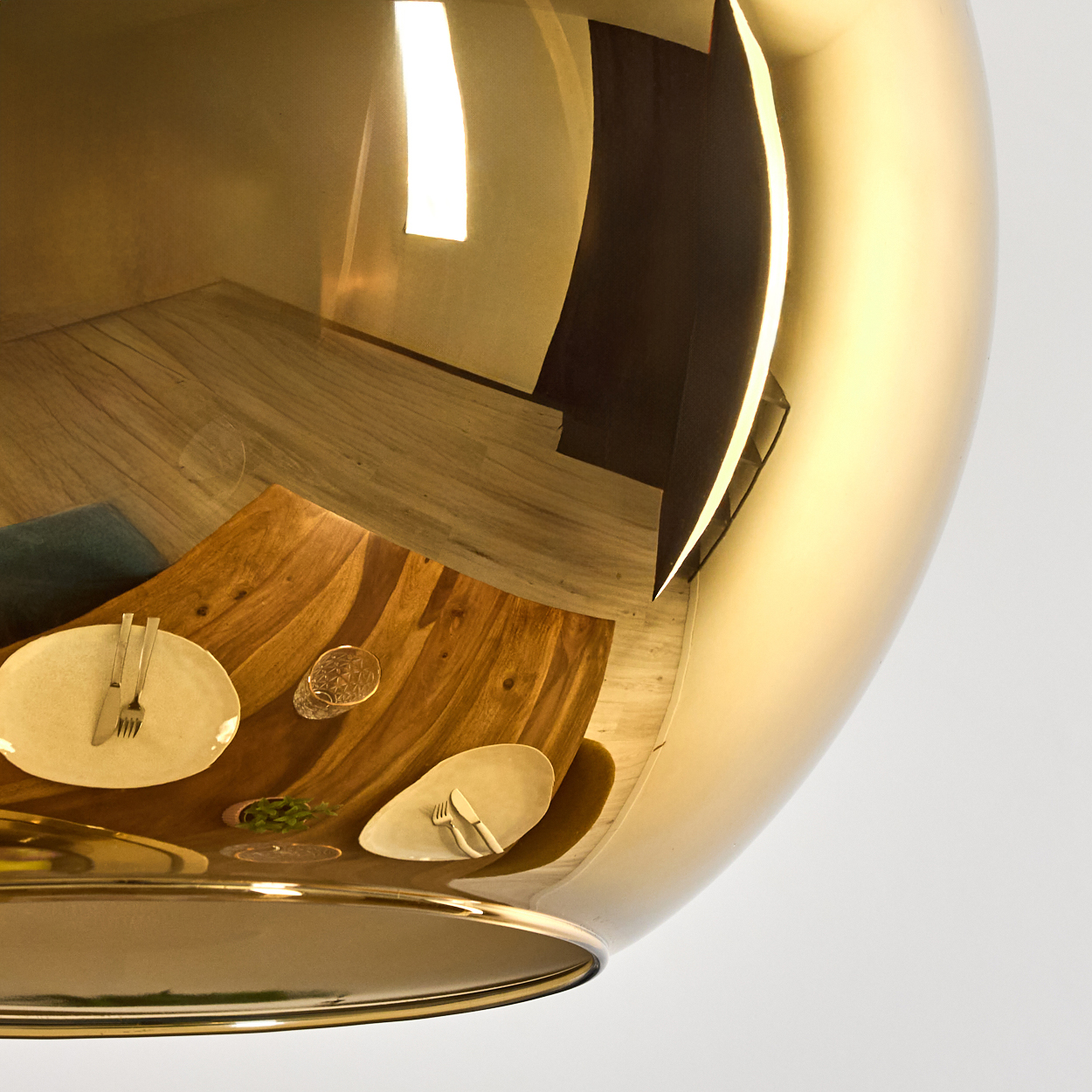 Eine goldene, reflektierende Leuchte mit einem Esstisch, der darauf reflektiert, mit Tellern, Besteck und einem Glas.