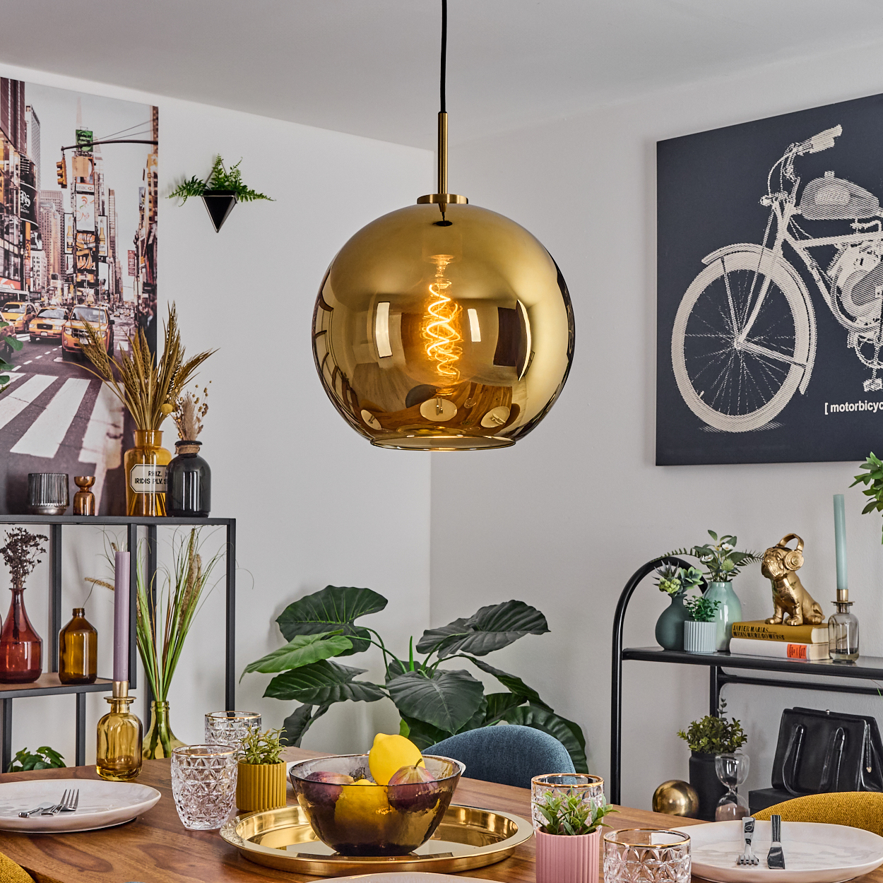 Esszimmer mit goldener Hängelampe. Tisch mit Obst und Gläsern gedeckt. Kunstwerk von Fahrrad und Stadtszene an den Wänden.