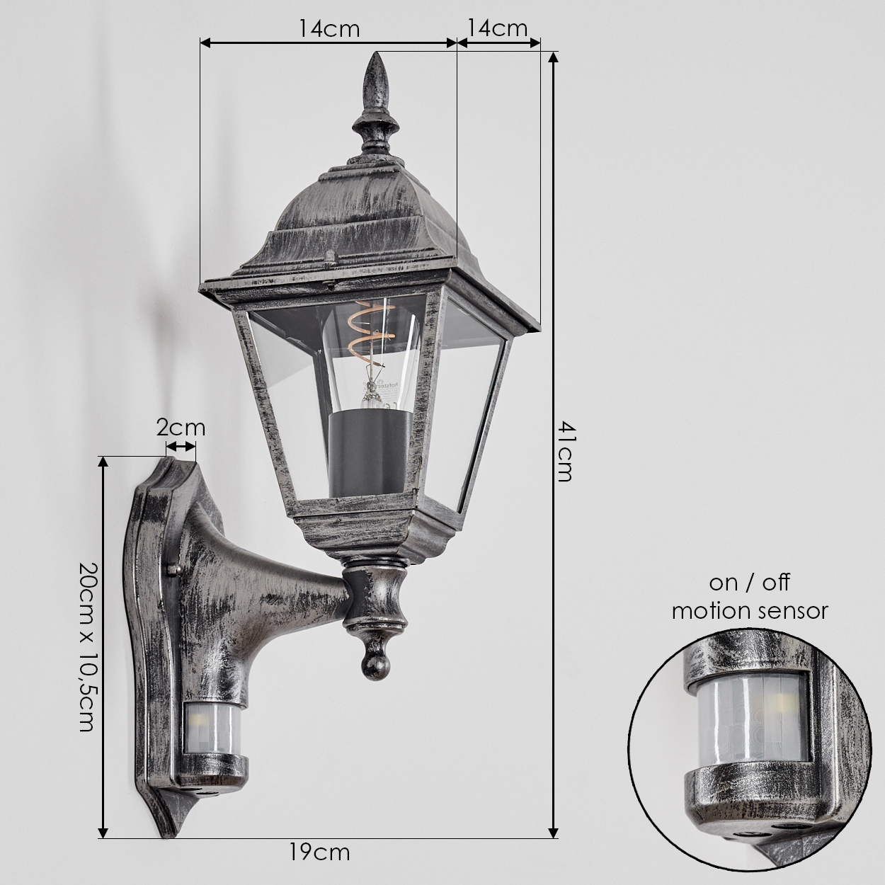 Eine metallische Außenlampe mit beschrifteten Abmessungen. Die Lampe hat einen Bewegungssensor und ist an einer weißen Wand befestigt.