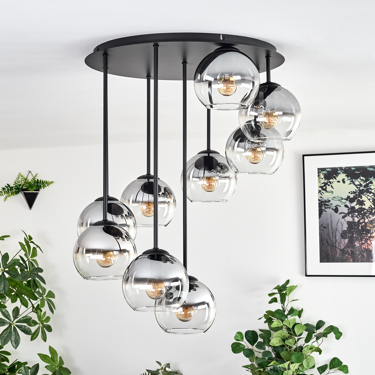 Eine moderne Deckenleuchte mit neun Glaskugelleuchten hängt von der Decke. Grüne Pflanzen und ein gerahmtes Bild schmücken die weiße Wand.