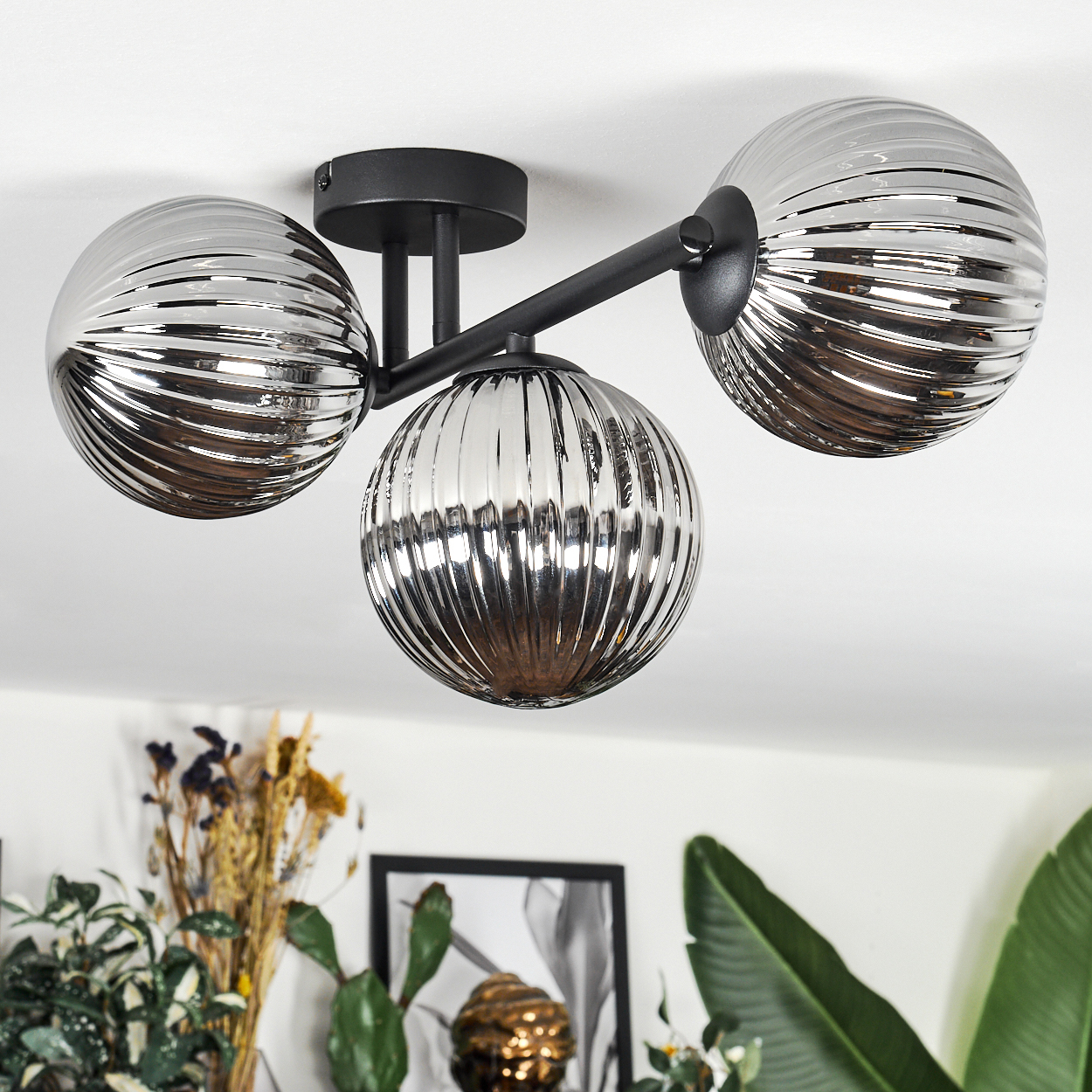 Eine moderne Deckenlampe mit drei kugelförmigen Schirmen. Die Schirme sind geriffelt und silberfarben. Die Lampe ist auf einem schwarzen Sockel montiert.