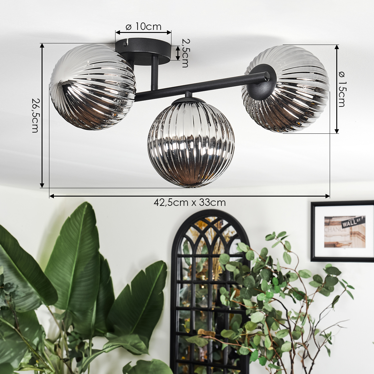 Moderne Deckenlampe mit drei kugelförmigen Schirmen. Abmessungen angegeben. Pflanzen und ein gerahmtes Bild im Hintergrund.