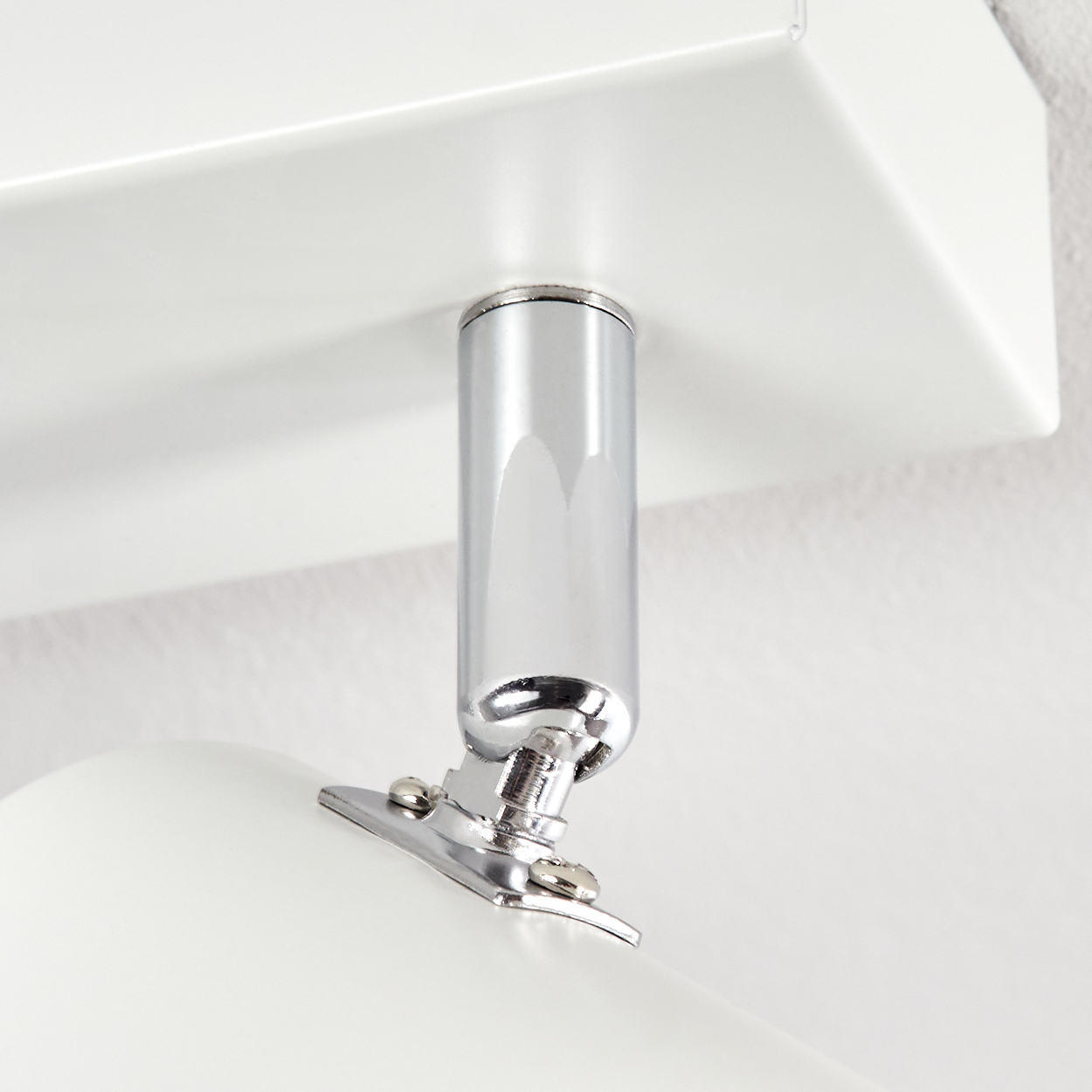 Nahaufnahme einer weißen Lampenhalterung. Ein Chromzylinder verbindet sich mit einer weißen Basis und einer weißen, abgerundeten Lampe. Der Hintergrund ist weiß.