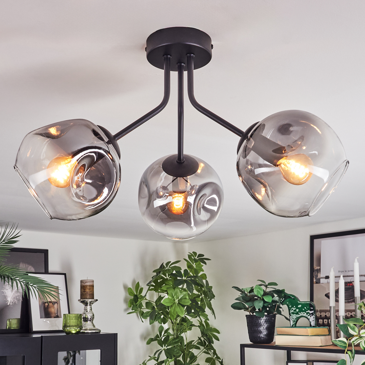 Eine moderne Deckenleuchte mit drei rauchigen Glasschirmen, jeweils mit einer warmen Glühbirne. Die Leuchte ist schwarz und an einer weißen Decke montiert.