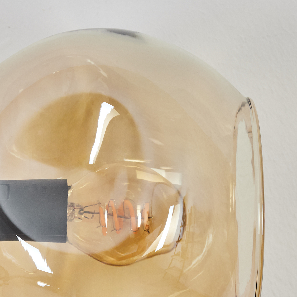 Nahaufnahme einer Leuchte mit Glasabdeckung. Im Glas befindet sich eine Glühbirne, das Glas ist orange. Der Hintergrund ist weiß.