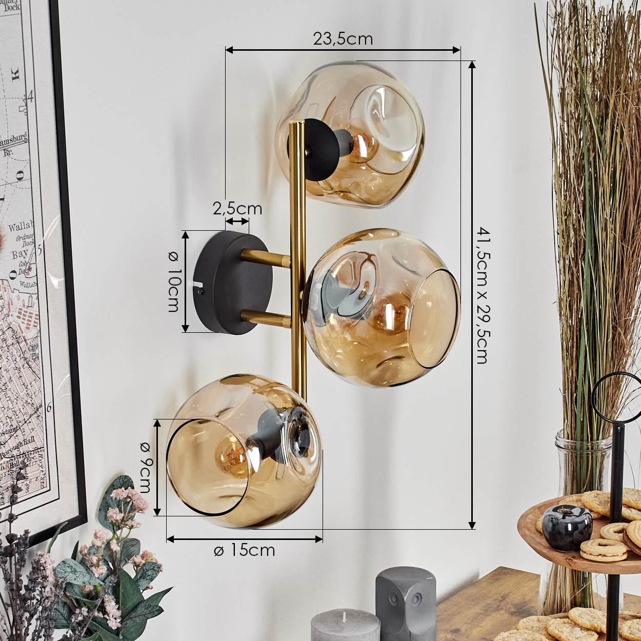 Eine Wandlampe mit drei Glaskugeln, goldenen Akzenten und schwarzem Sockel. Abmessungen sind angegeben. Hintergrund enthält Deko und eine Karte.