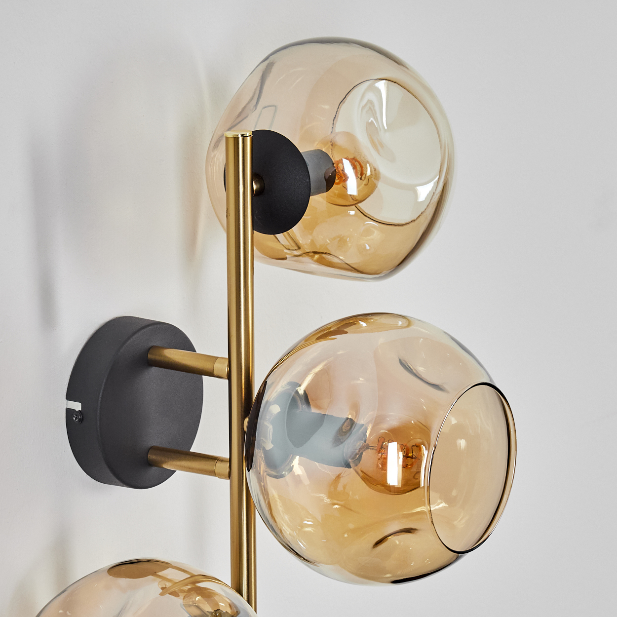 Eine moderne Wandlampe mit drei bernsteinfarbenen Glaskugeln. Die Lampe ist an einer weißen Wand mit schwarzem und goldenem Akzent befestigt.