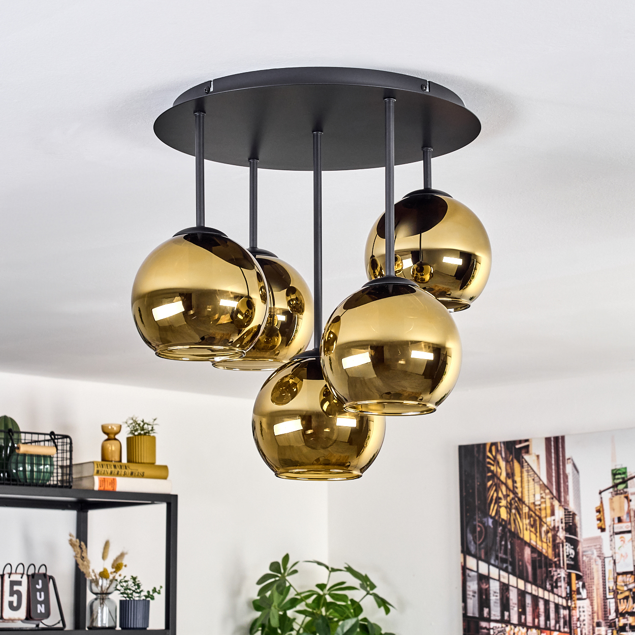 Fünf goldene Kugeln hängen an einer schwarzen Deckenleuchte. Die Decke ist weiß, und es gibt andere dekorative Gegenstände im Raum.
