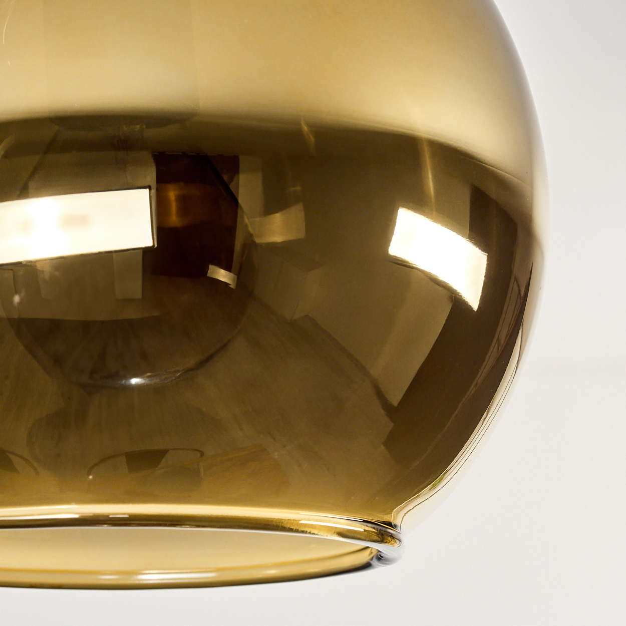 Nahaufnahme eines goldenen Glasschirmes. Er reflektiert Licht und die Umgebung vor weißem Hintergrund.