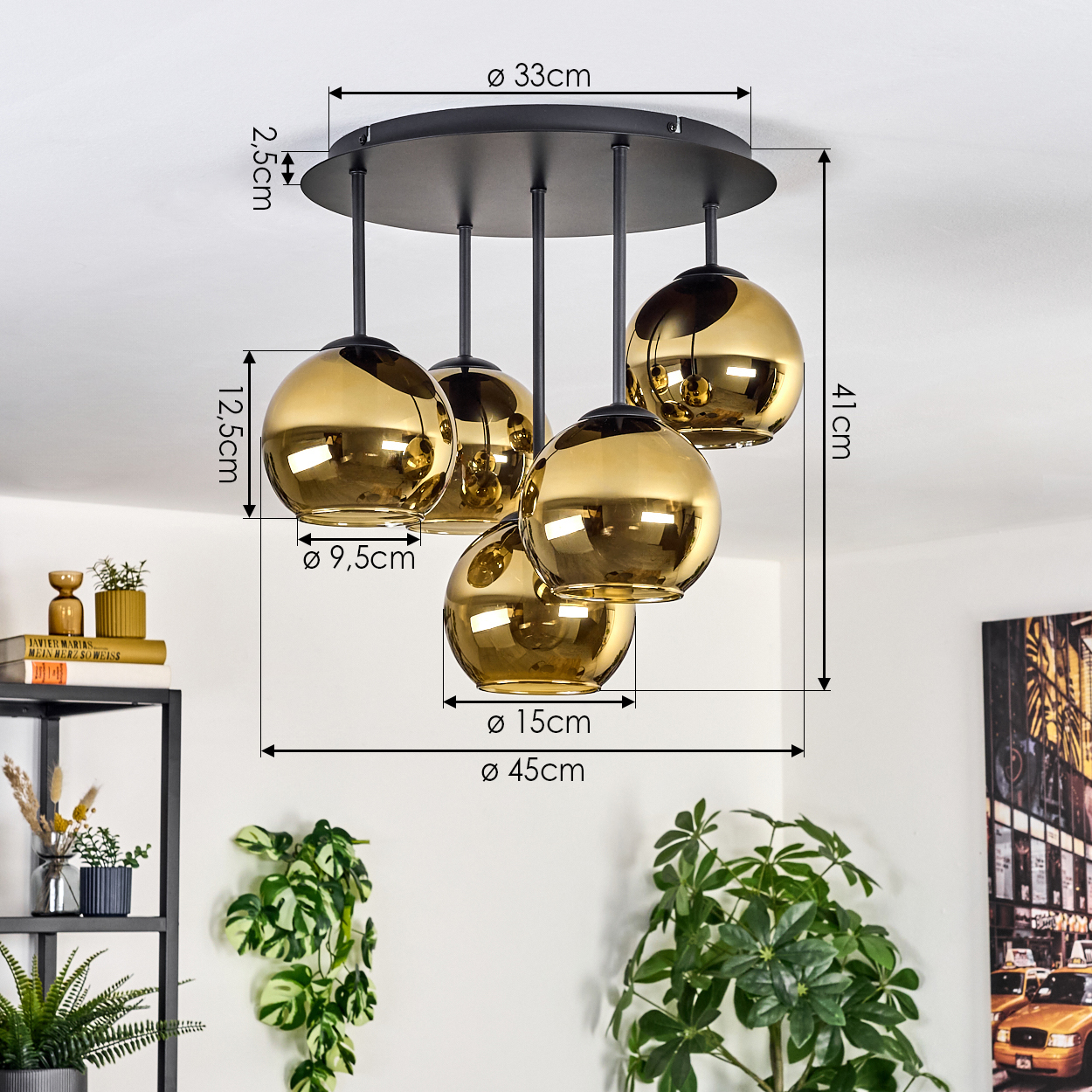 Eine Pendelleuchte mit fünf goldfarbenen Kugeln hängt von der Decke. Maße sind angegeben. Pflanzen und Dekoration sind im Hintergrund.