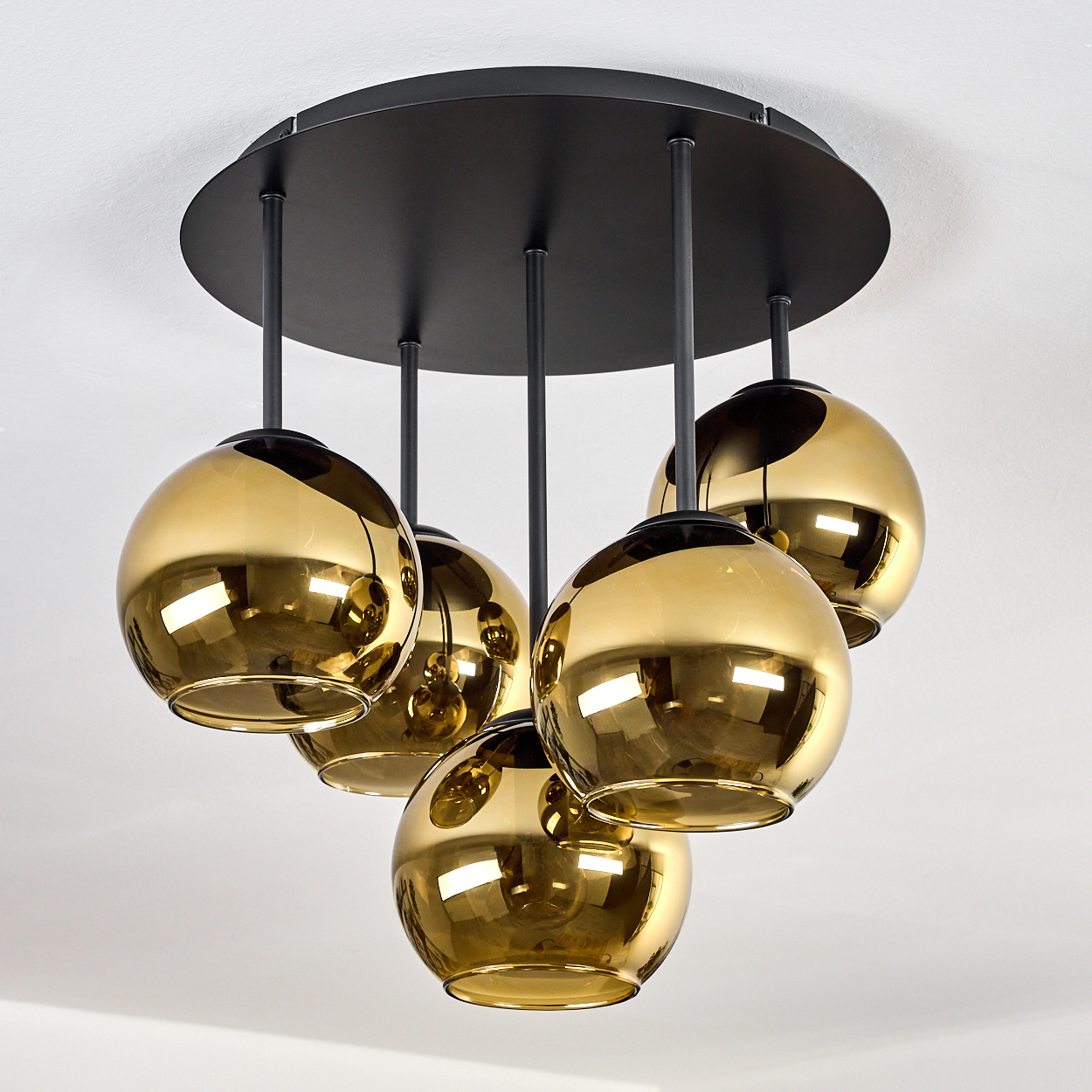 Moderne Deckenlampe mit fünf goldenen Glaskugeln, die von einer schwarzen runden Basis abgehängt sind, vor weißer Decke.