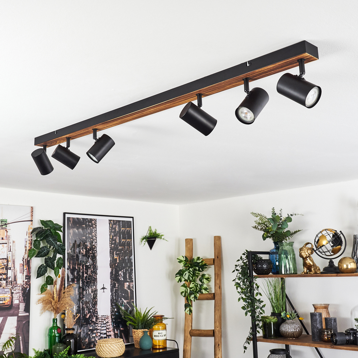 Schwarze Deckenstrahler an Holzbalken. Raum mit Dekor, Pflanzen, Leiter und Kunstwerk. Weiße Wände und Decke.