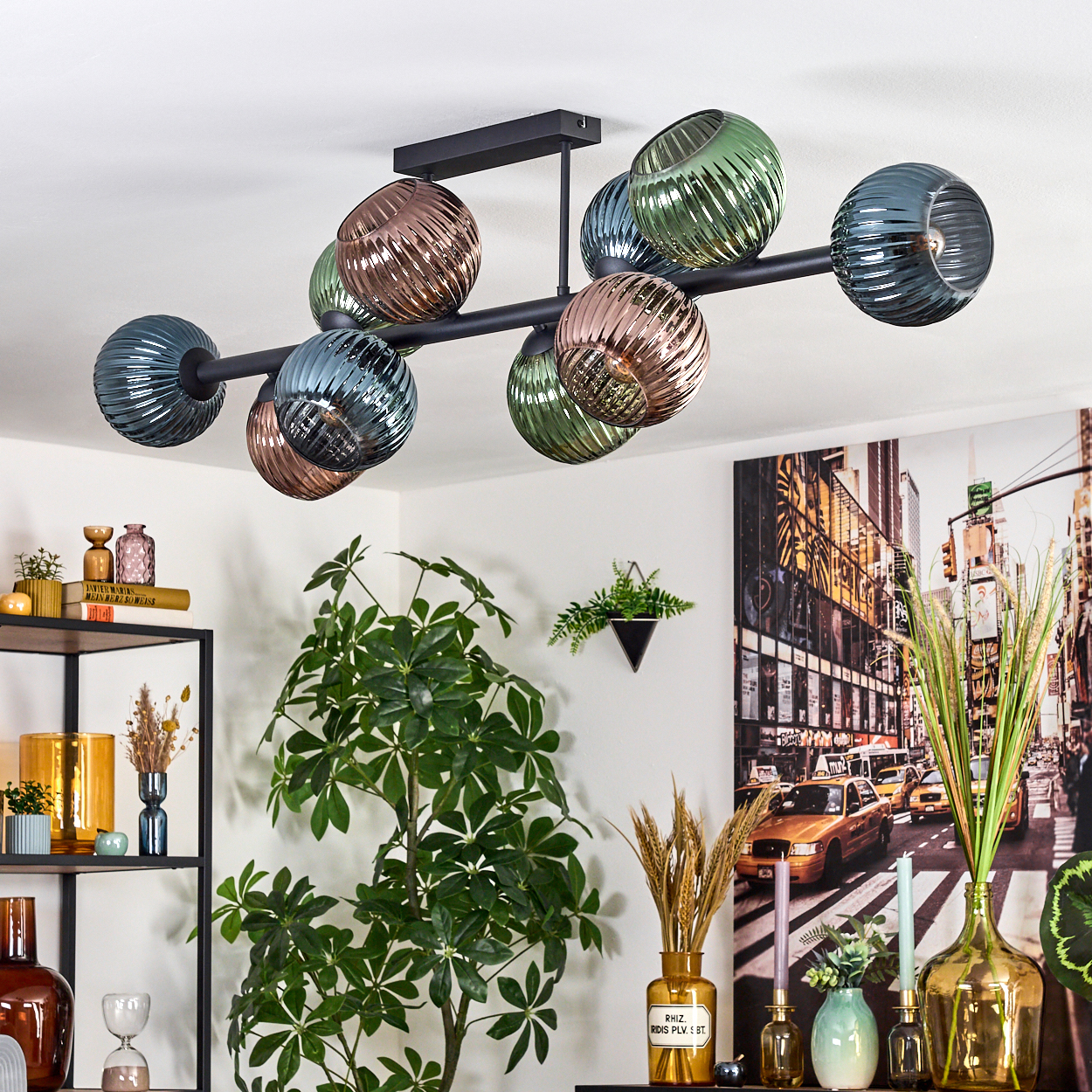Eine moderne schwarze Deckenlampe mit bunten Glaskugeln. Im Hintergrund verschiedene Pflanzen und ein Stadtbildgemälde.
