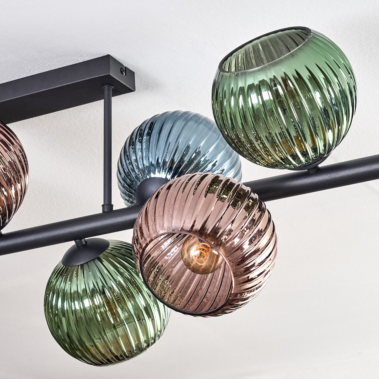 Eine moderne Deckenleuchte mit runden, geriffelten Glasschirmen in verschiedenen Farben: Grün, Blau, Rosa und klar, mit einem schwarzen Metallrahmen.