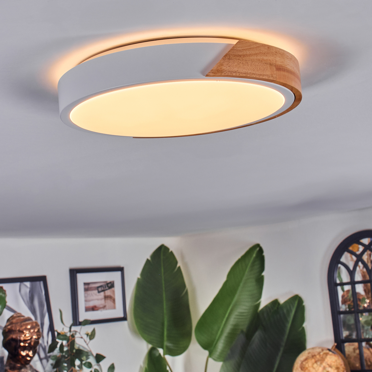 Eine moderne Deckenleuchte mit Holz- und Weißdesign. Darunter befinden sich Pflanzen, Bilder und ein dekorativer Globus.
