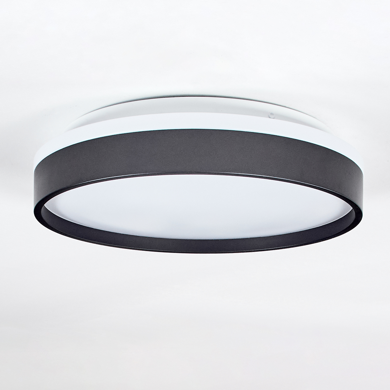 Eine moderne Deckenleuchte, kreisförmig, mit einem schwarzen Band um die Mitte. Das Licht ist innen weiß und der Hintergrund ist weiß.