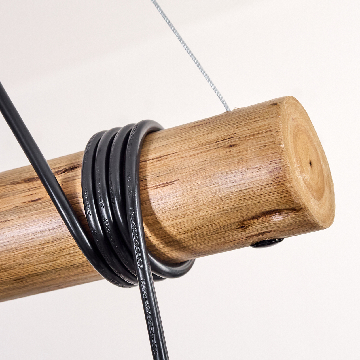 Holzbalken mit schwarzem Kabel umwickelt, an einem Draht hängend, vor weißem Hintergrund.