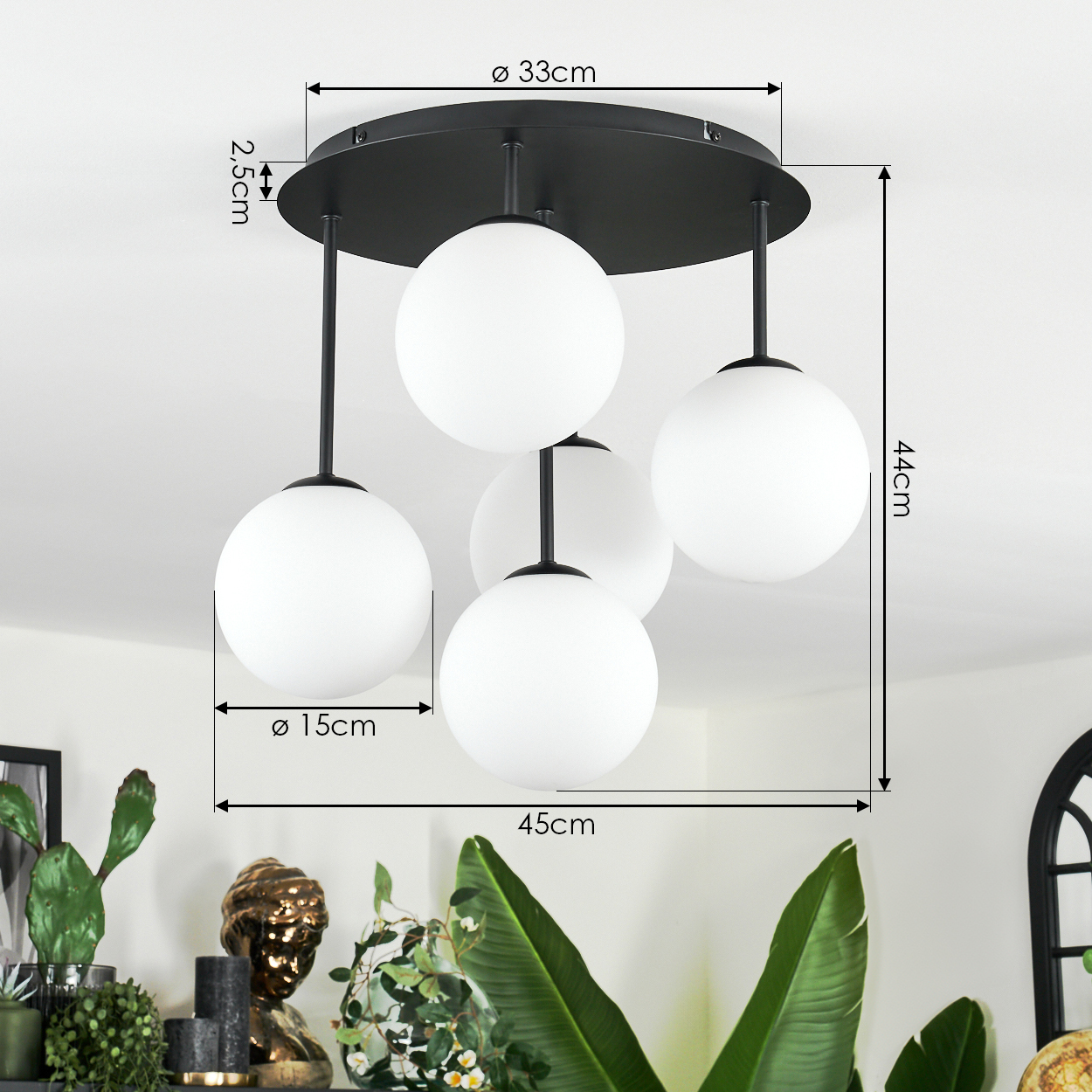 Eine moderne Deckenlampe mit vier weißen Kugeln. Schwarze Stäbe verbinden die Kugeln mit einer schwarzen kreisförmigen Basis. Pflanzen und eine Büste sind im Vordergrund.