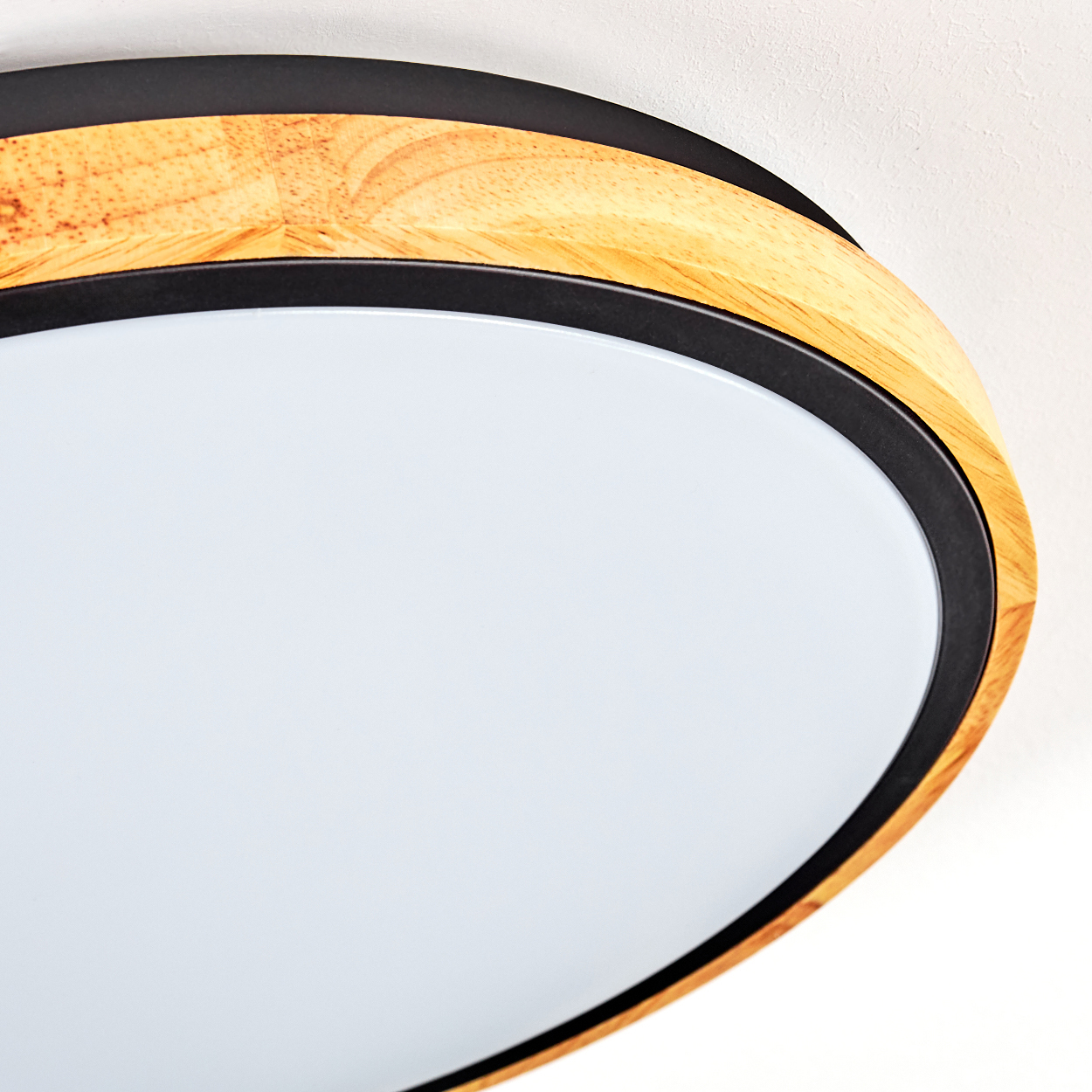 Nahaufnahme einer Deckenleuchte. Sie hat einen Holzrahmen mit einem schwarzen Ring und ein weißes, rundes Lichtpanel. Der Hintergrund ist weiß.
