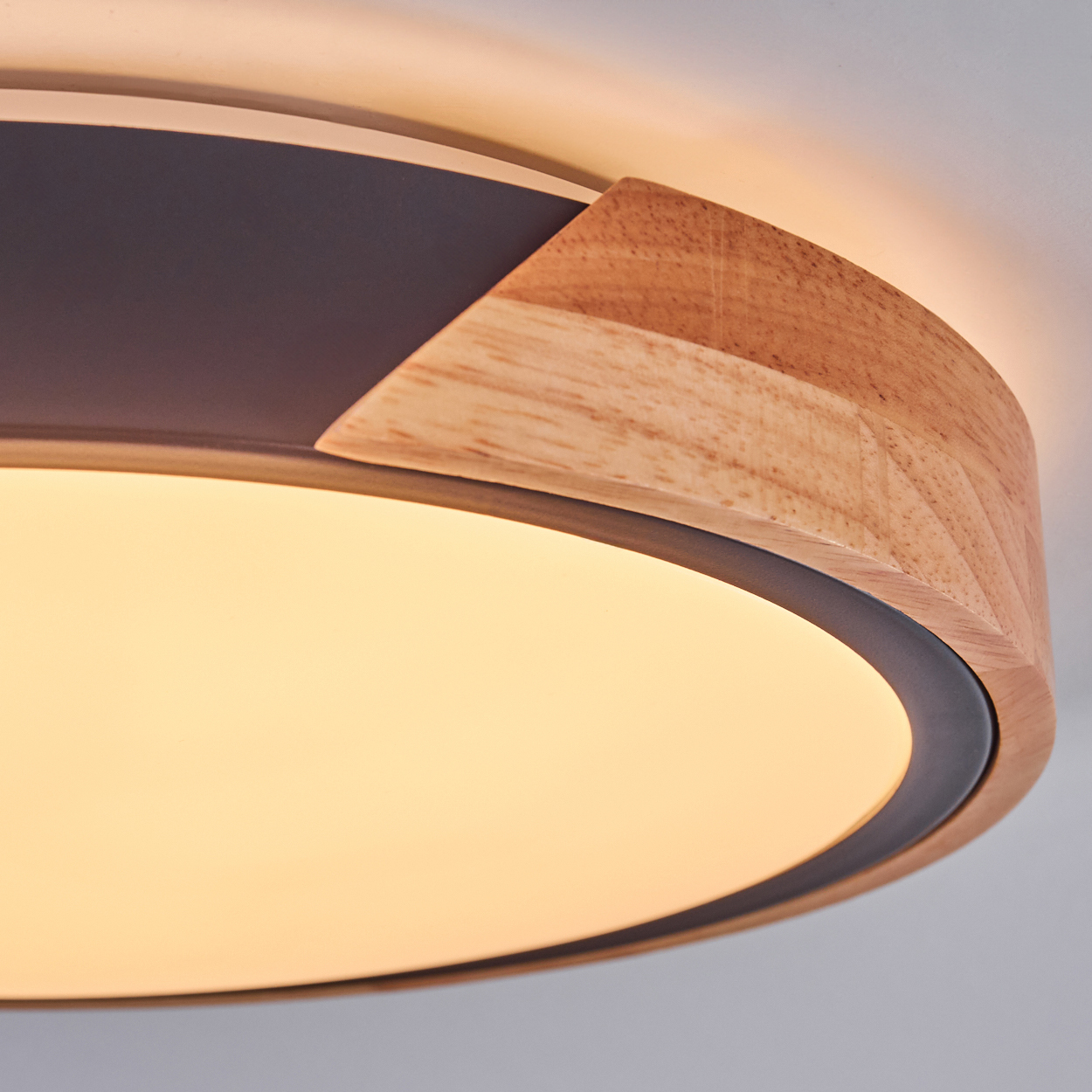 Nahaufnahme einer modernen Deckenleuchte mit Holzrahmen und heller, kreisförmiger Lichtquelle. Der Hintergrund ist weiß.