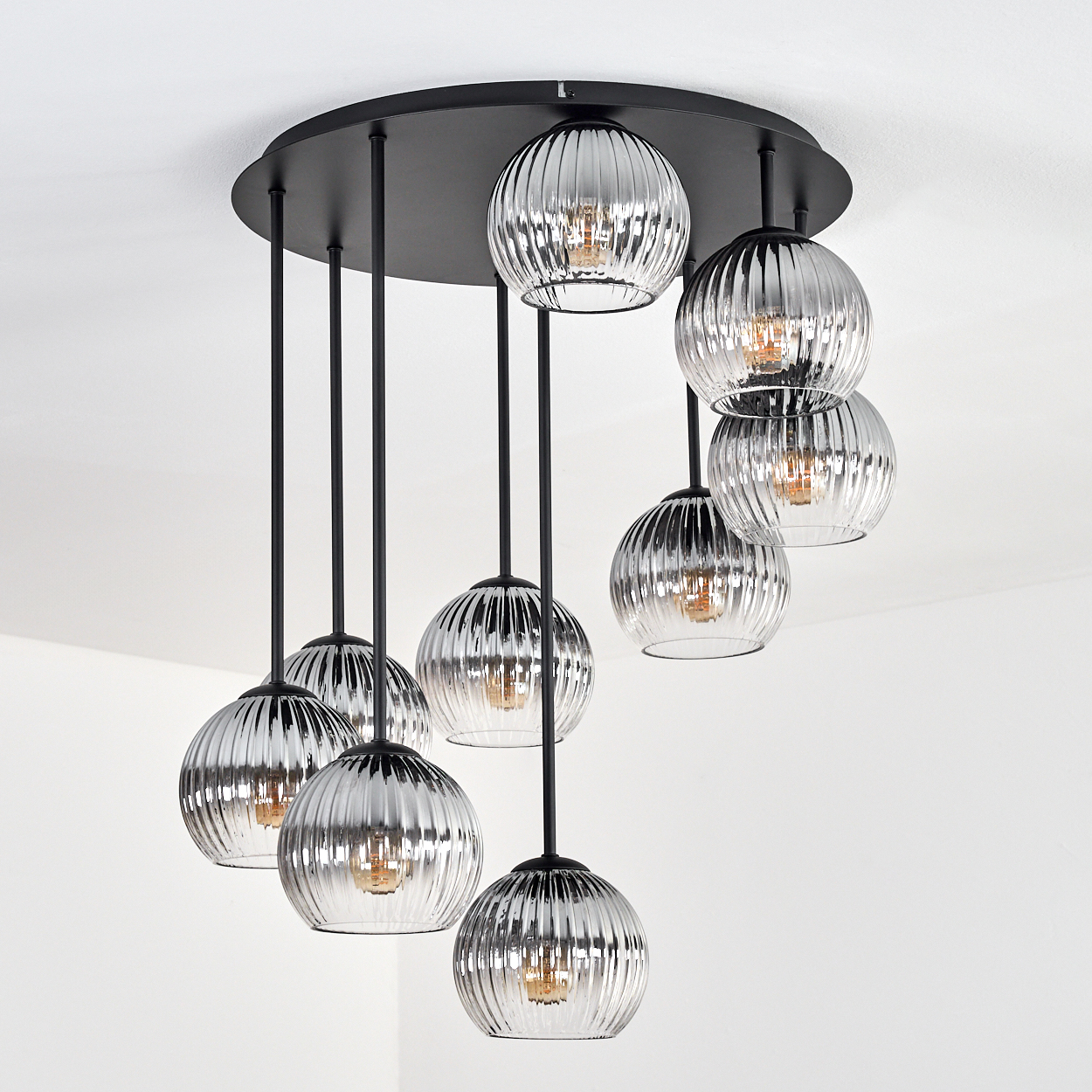 Eine moderne Deckenleuchte mit neun kugelförmigen, gerippten Glasschirmen, die an schwarzen Stäben und einem schwarzen kreisförmigen Sockel hängen.