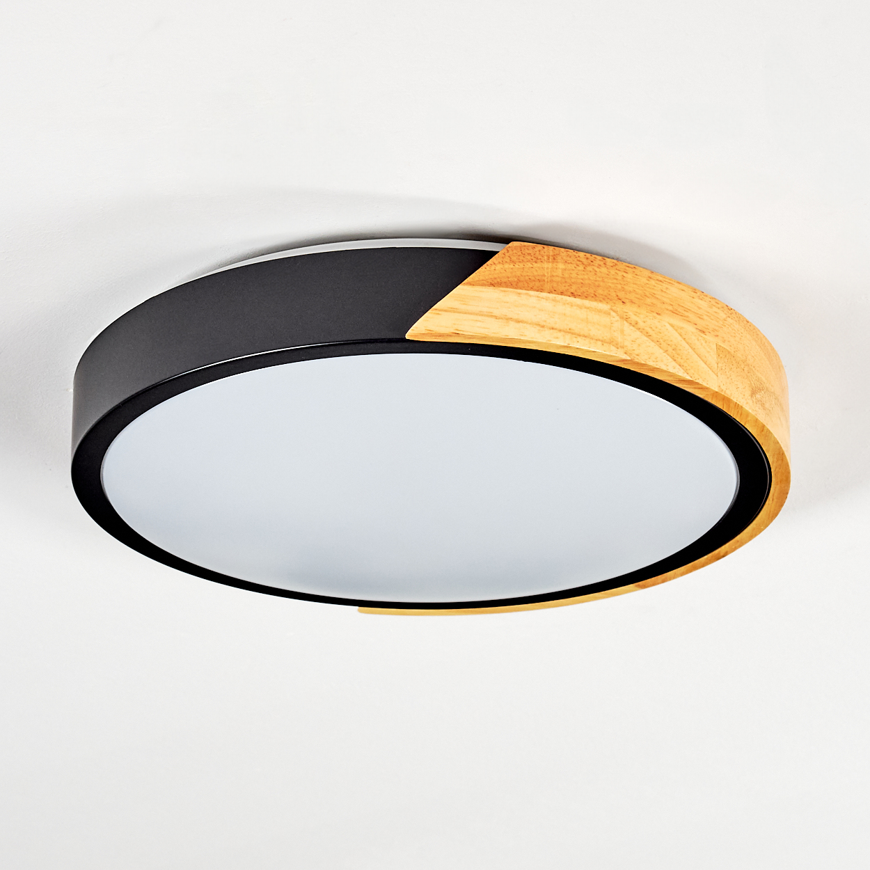 Eine runde Deckenlampe. Sie hat einen schwarzen Metallrahmen mit Holzakzent und einen weißen Lichtdiffusor. Der Hintergrund ist weiß.