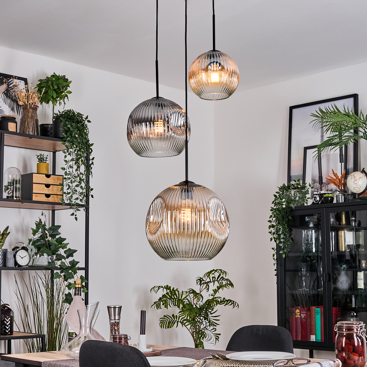 Esszimmer mit drei Hängelampen. Regale mit Pflanzen und Dekor. Ein Tisch zum Essen mit einem Glasschrank.