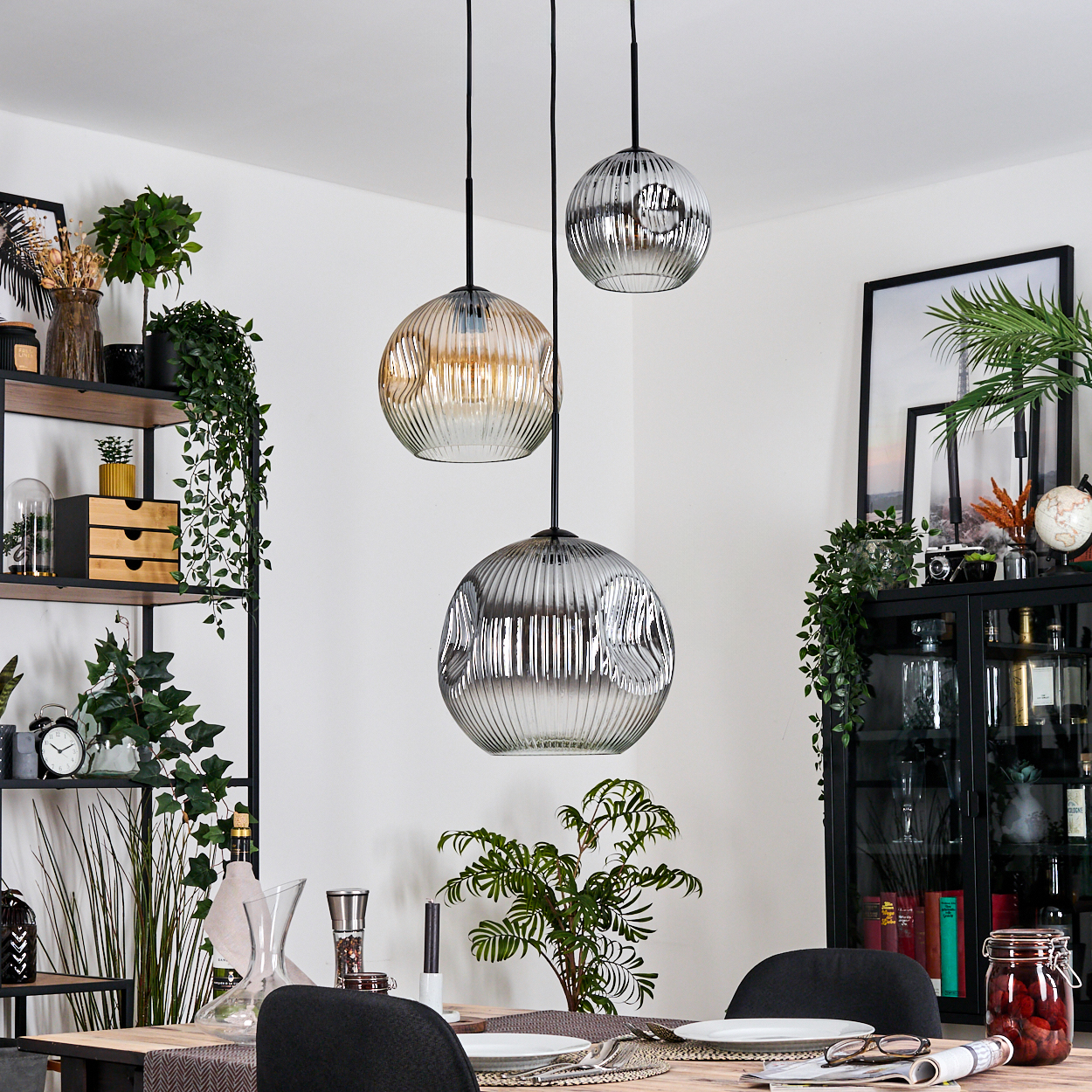 Drei runde, gerippte Glas-Pendelleuchten hängen über einem Esstisch. Pflanzen und Dekoration sind im Hintergrund sichtbar.