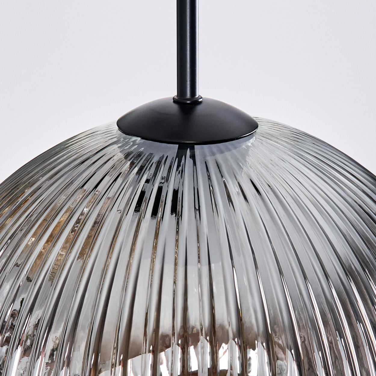 Nahaufnahme eines Lampenschirms aus Glas mit vertikalen Rippen. Schwarze Metallhalterung oben. Weißer Hintergrund.