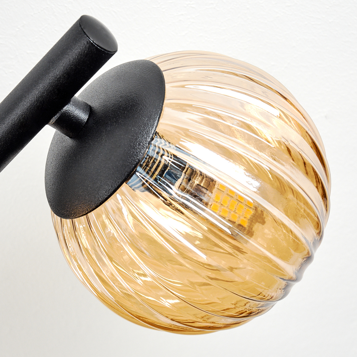 Nahaufnahme einer Lampe. Sie hat einen schwarzen Arm und einen runden, bernsteinfarbenen Glasschirm mit strukturierter Oberfläche. Der Hintergrund ist weiß.
