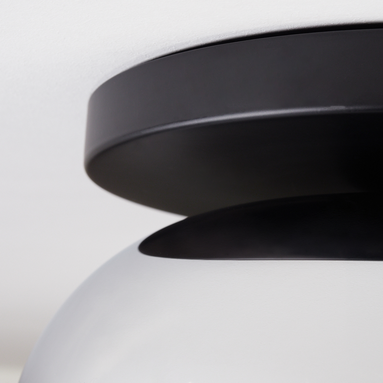 Nahaufnahme einer modernen Lampe. Die Oberseite ist schwarz, die Unterseite weiß. Der Hintergrund ist eine weiße Decke.