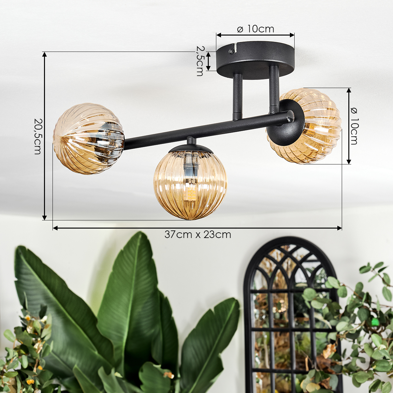 Moderne schwarze Deckenlampe mit drei bernsteinfarbenen Glaskugeln. Maße sind angezeigt. Pflanzen und ein Spiegel im Hintergrund.