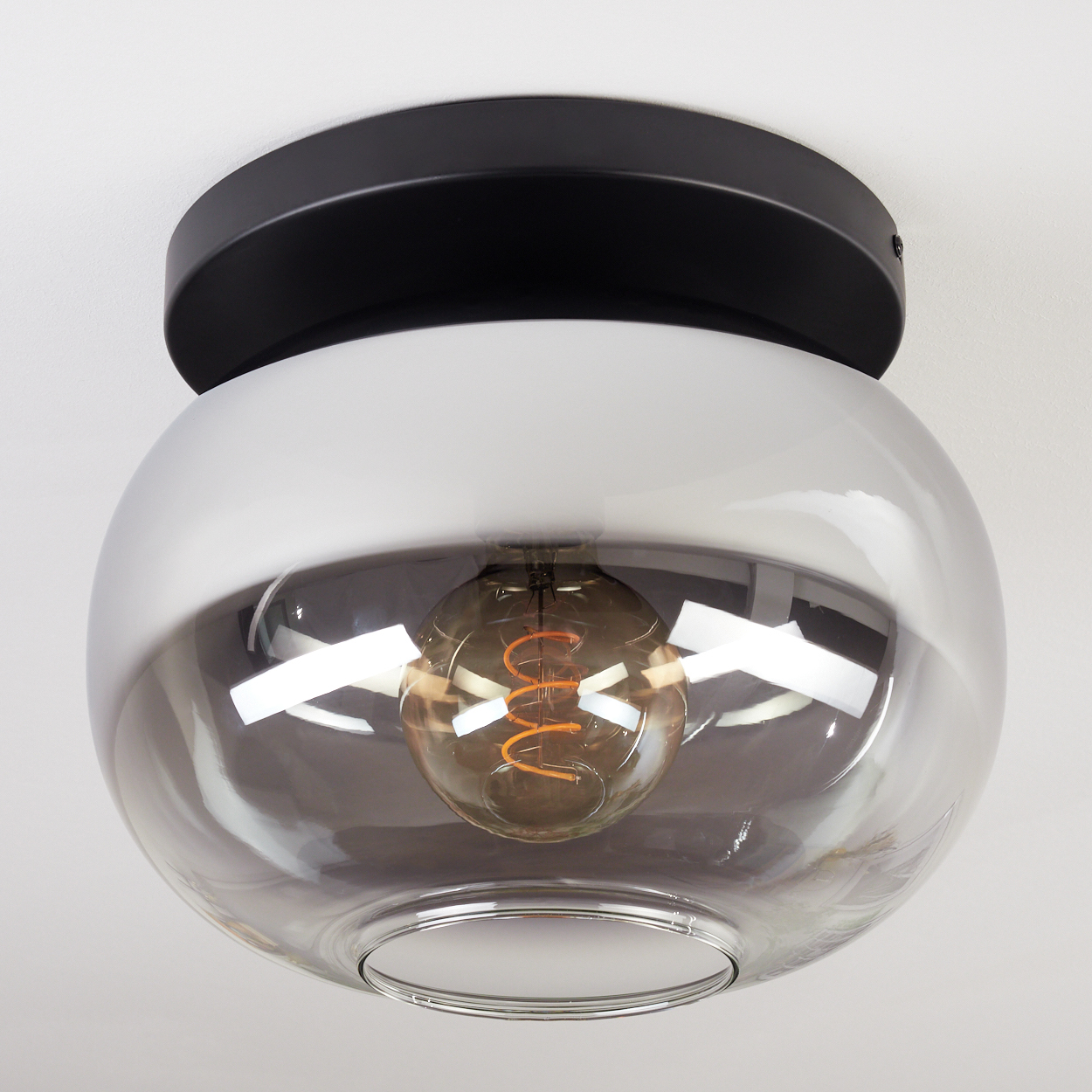Moderne Deckenleuchte. Sie hat einen schwarzen Sockel, einen weißen Mittelteil und ein klares, rundes Glas mit einer sichtbaren Glühbirne.