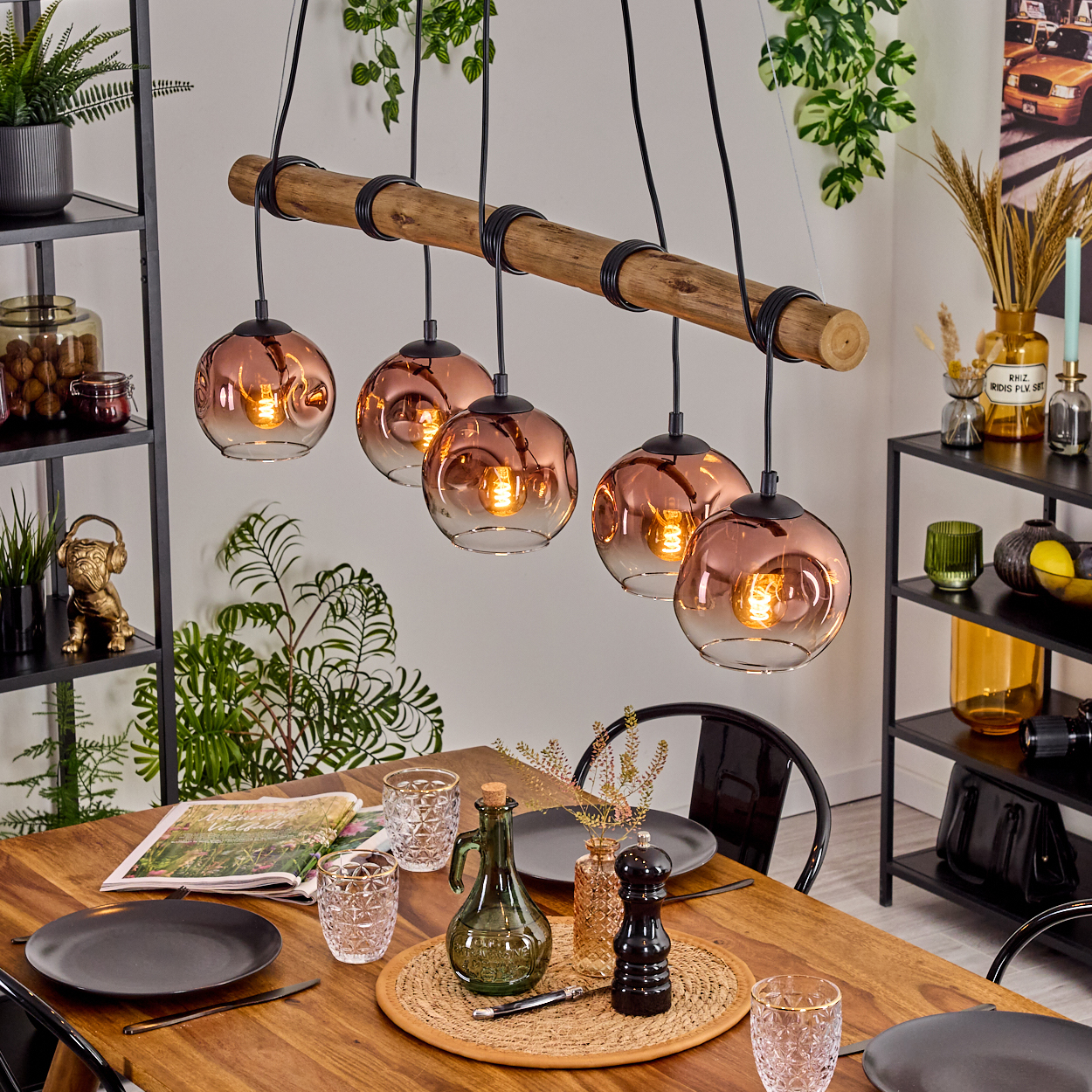 Ein Esszimmer mit einem Holztisch, der zum Abendessen gedeckt ist. Darüber hängen sechs kupferfarbene Kugelleuchten. Regale mit Dekor sind sichtbar.