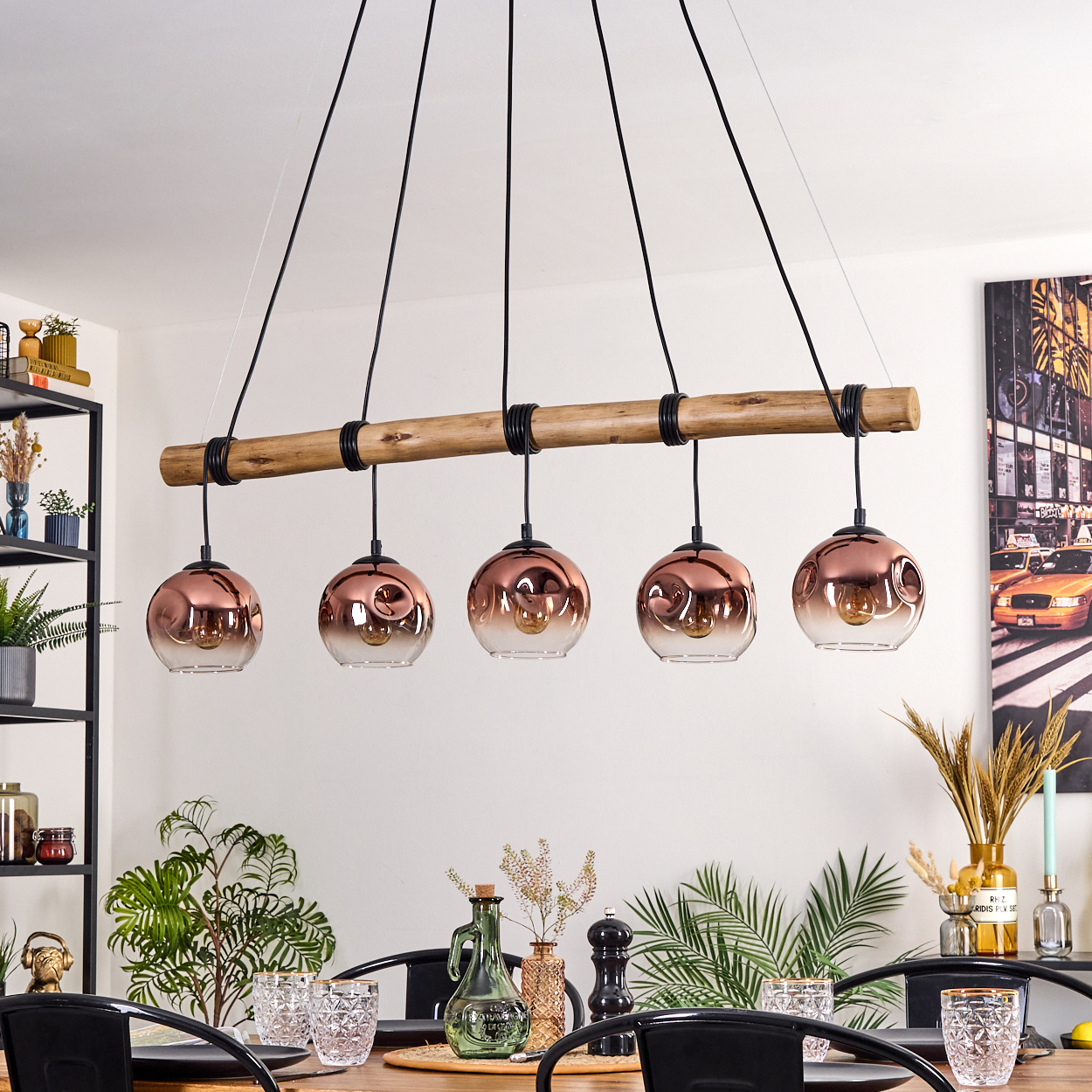 Ein Esszimmer mit Holztisch, Hängelampen und Pflanzen. Im Hintergrund ein Gemälde einer Stadtszene.