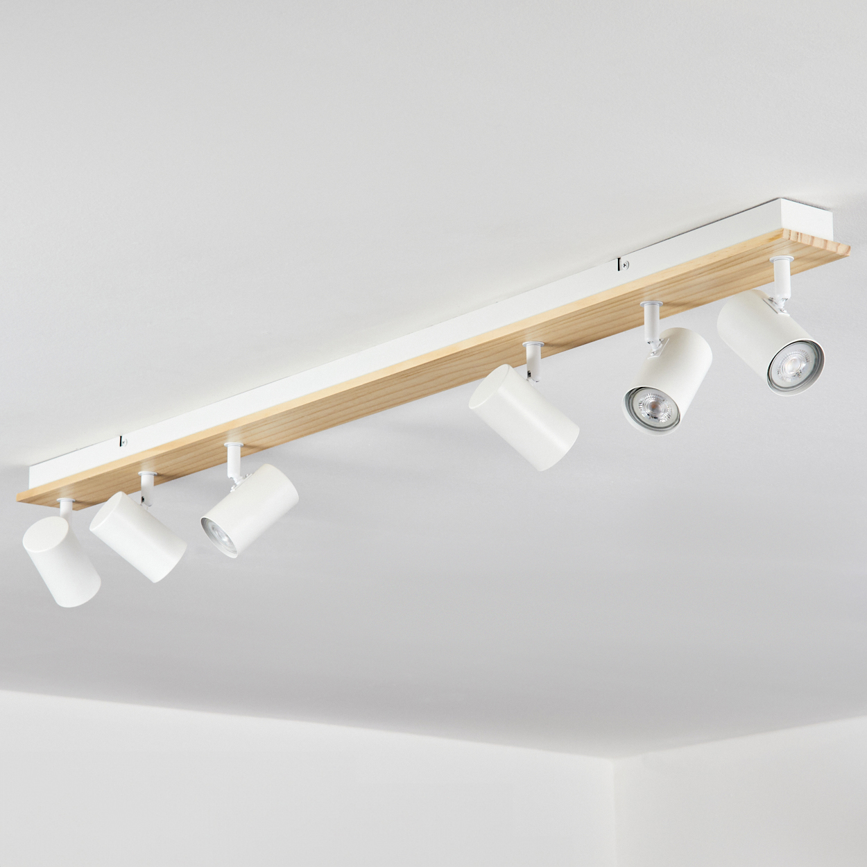 An der Decke montierte Leuchte. Weiße Strahler auf einer Holzplatte, an der Decke befestigt. Die Decke ist weiß.