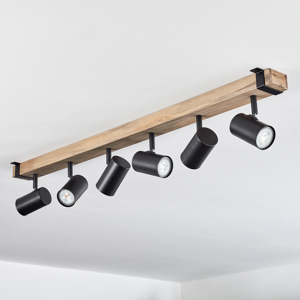 Eine Deckenleuchte mit sechs schwarzen Strahlern, die an einem Holzbalken befestigt sind. Der Hintergrund ist eine weiße Decke.