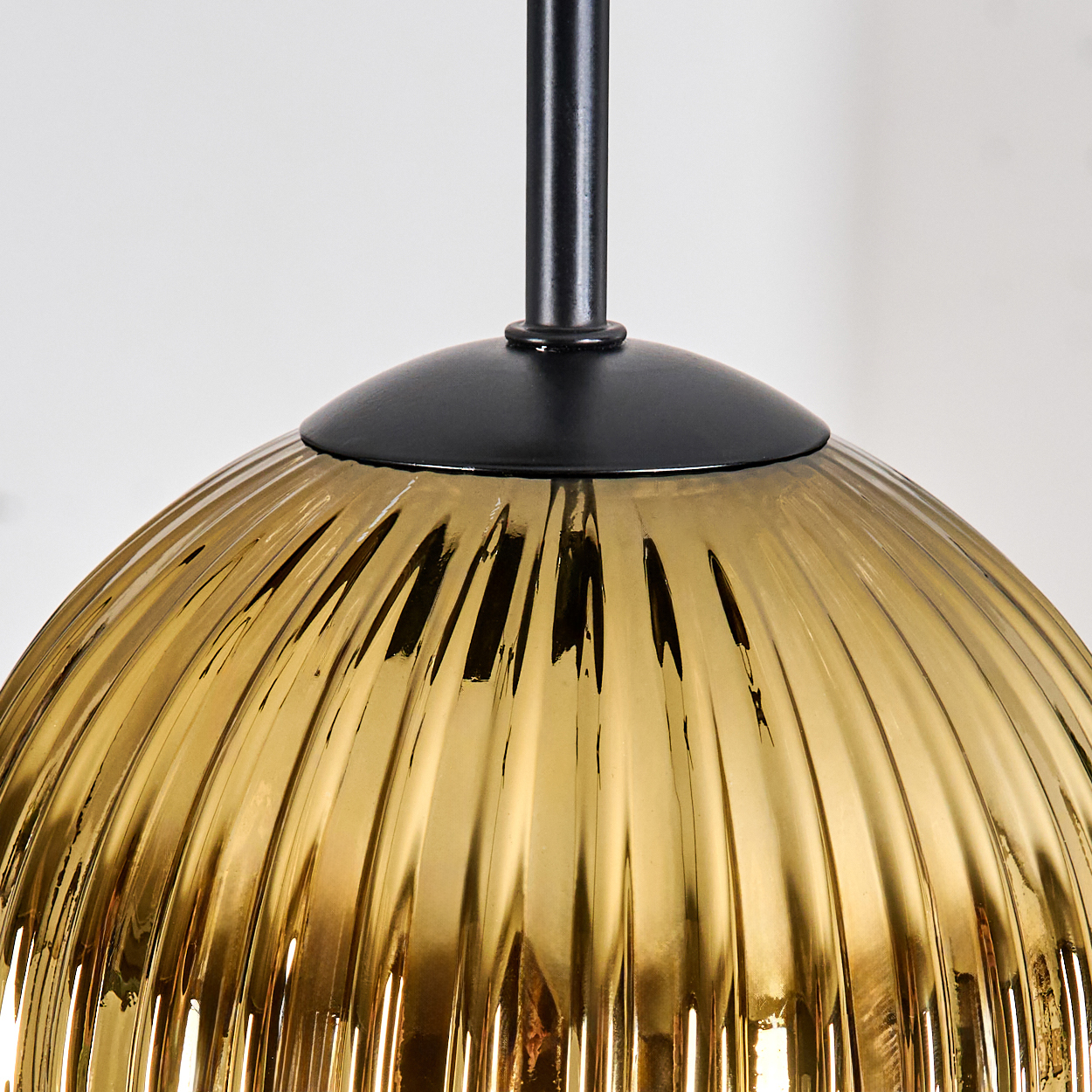 Nahaufnahme eines goldenen, gerippten Glaslampenschirms mit schwarzem Stiel und Kappe. Der Hintergrund ist eine weiße Wand.