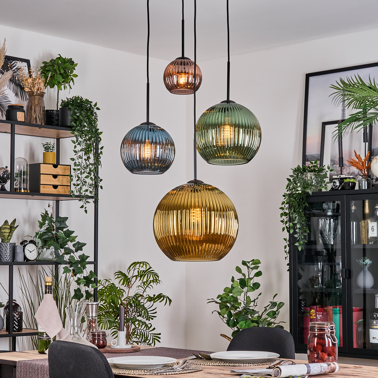 Esszimmer mit vier bunten Pendelleuchten, Tisch für zwei Personen und Pflanzen auf Regalen und Schränken.