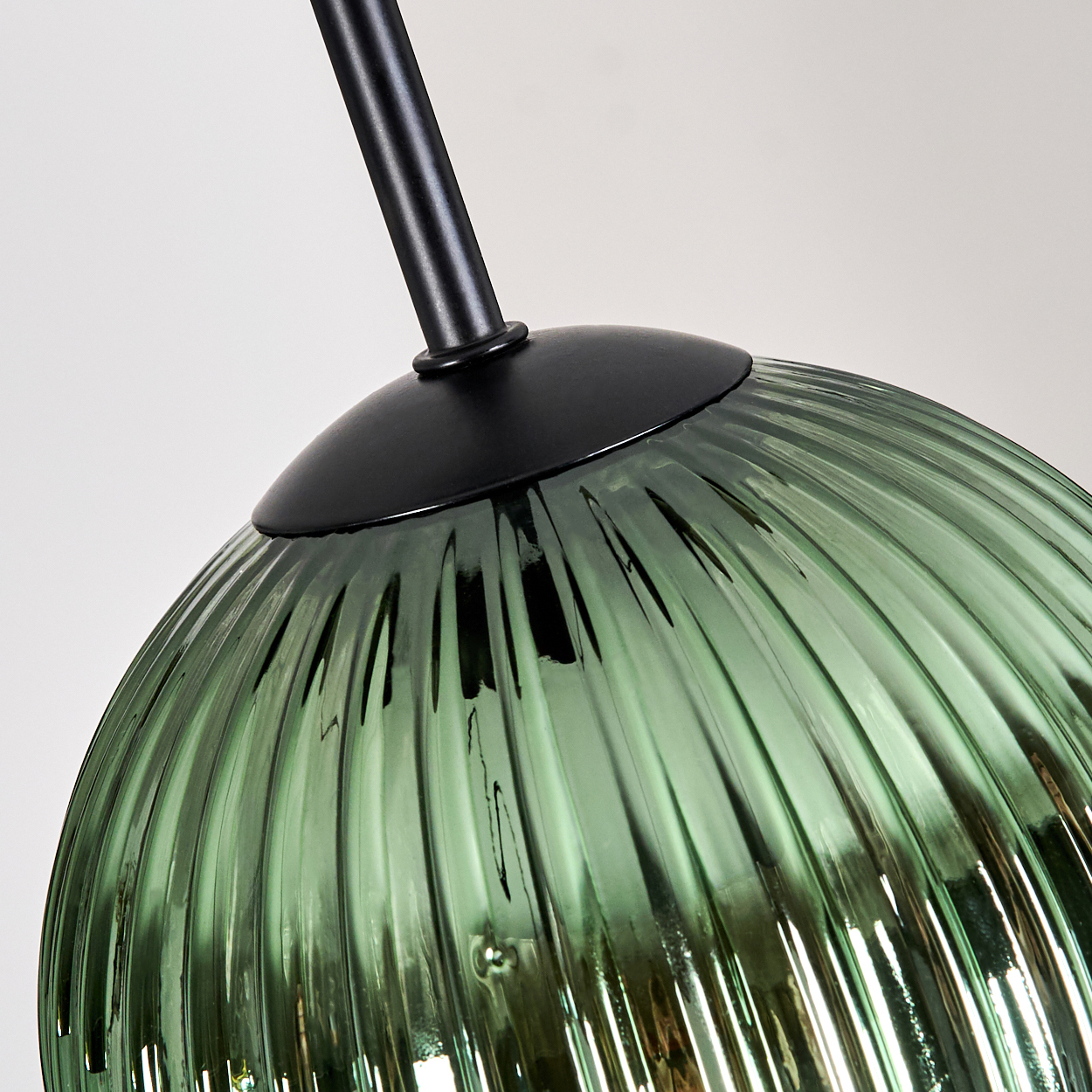 Nahaufnahme eines grünen, gerippten Glasschirms mit schwarzem Stiel vor weißem Hintergrund.