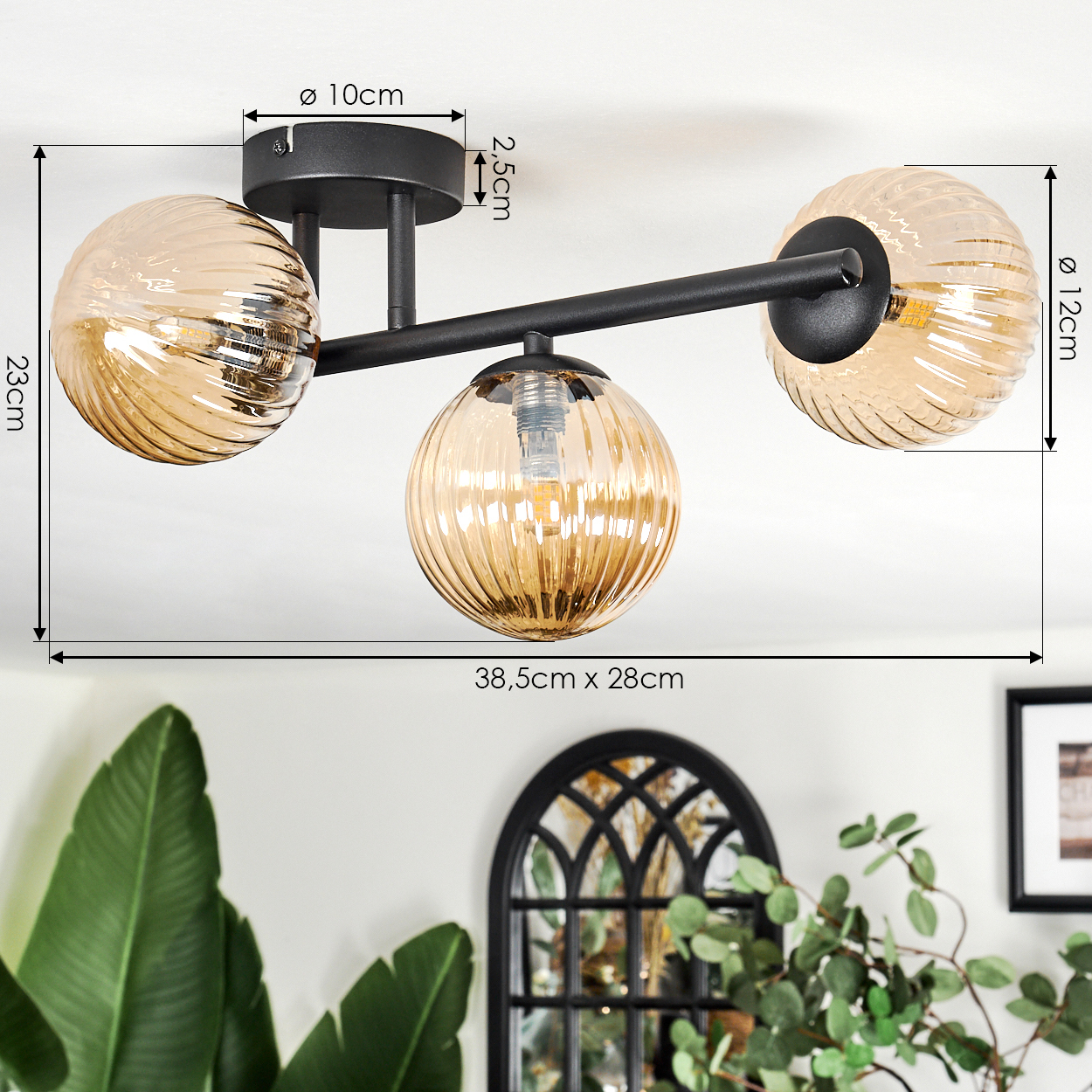 Eine moderne Deckenlampe mit drei bernsteinfarbenen Glasschirmen. Abmessungen sind angegeben. Im Hintergrund Pflanzen und ein dekorativer Spiegel.