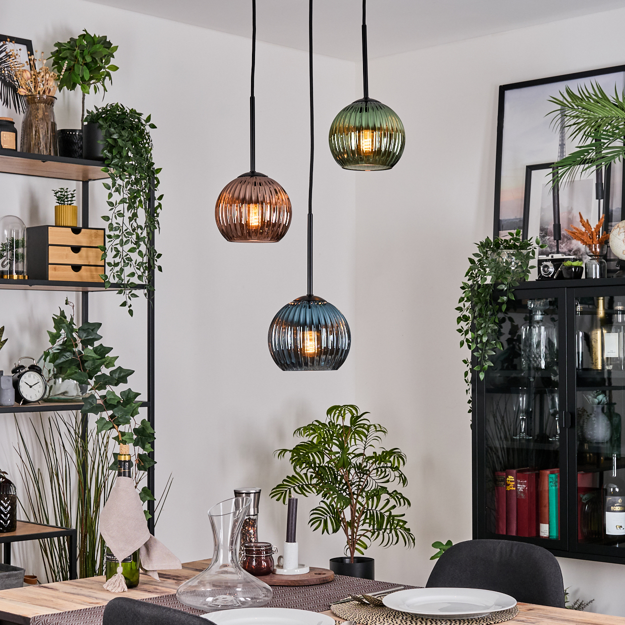 Esszimmer mit drei Hängelampen. Es gibt einen Tisch, Pflanzen und einen Schrank mit Dekorationen. Die Lichter haben verschiedene Farben.