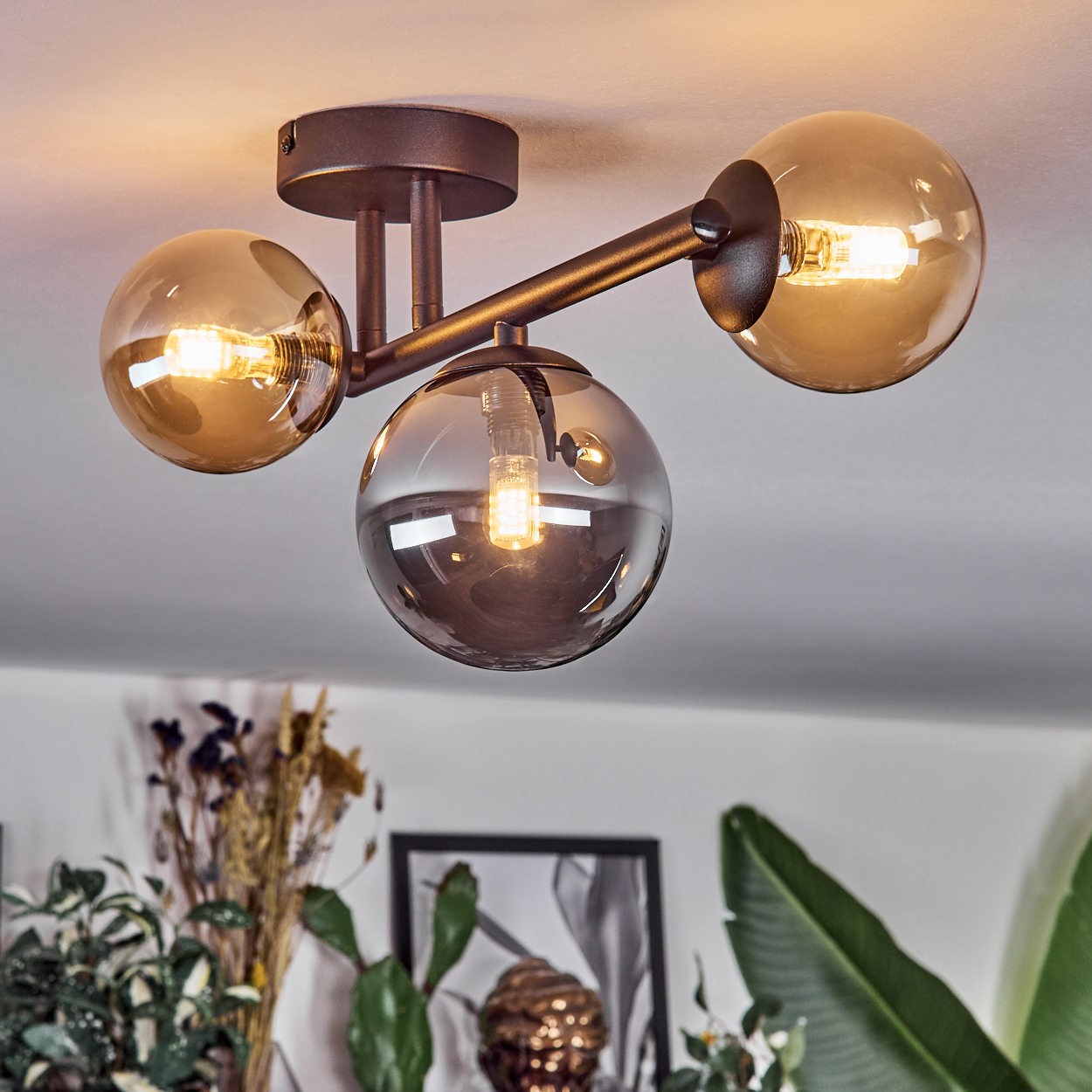 Eine moderne Deckenleuchte mit drei kugelförmigen Glasschirmen, die jeweils eine brennende Glühbirne enthalten. Die Leuchte ist an einer weißen Decke befestigt.