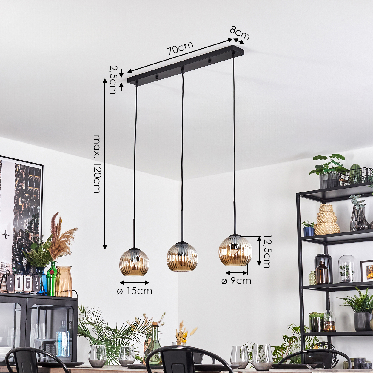 Drei Pendelleuchten mit Glasschirmen hängen an einer schwarzen Halterung. Abmessungen sind beschriftet. Pflanzen und ein Regal im Hintergrund.