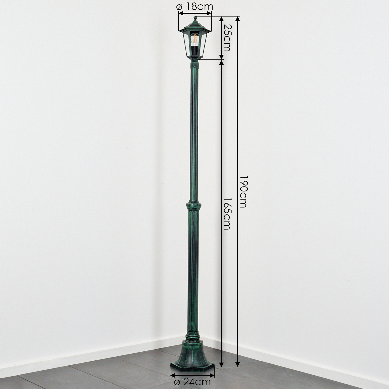 Eine grüne Außenlaterne mit Maßangaben. Die Lampe steht vor einer weißen Wand und einem grauen Boden.