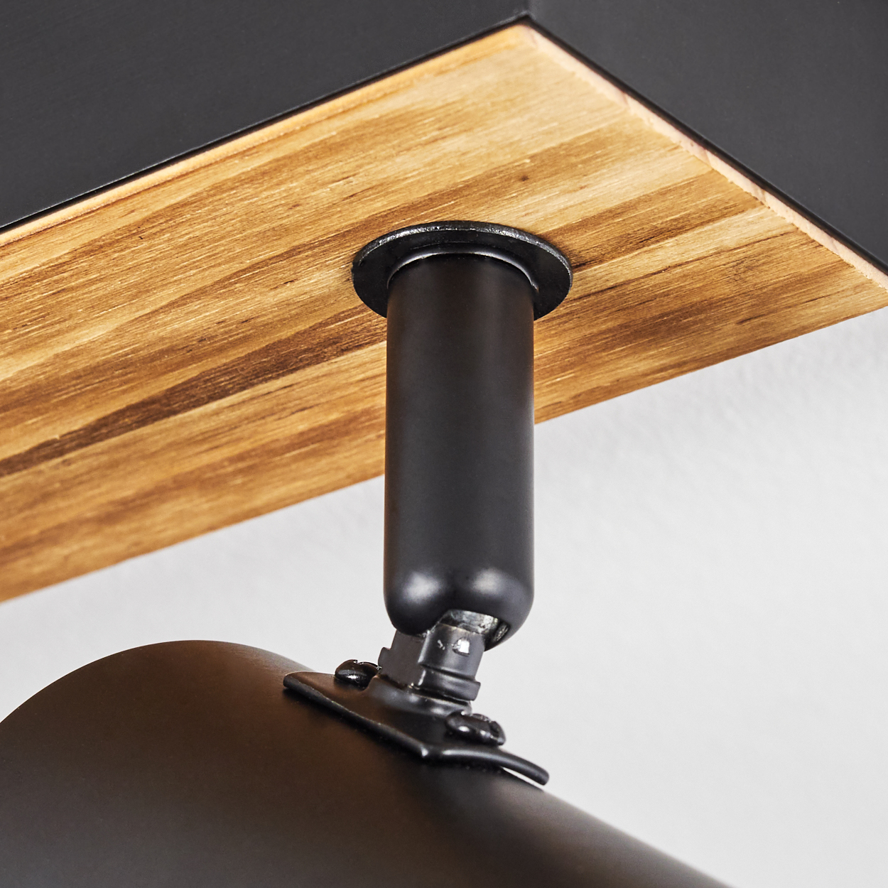 Nahaufnahme einer schwarzen Metalllampenhalterung, die an einer Holzoberfläche befestigt ist. Die Halterung ist abgewinkelt, mit einer schwarzen zylindrischen Lampe darunter.