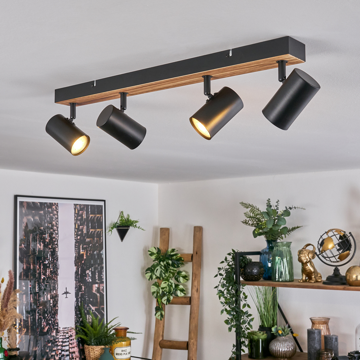 Deckenstrahler mit schwarzen Leuchten, Holzbalken und hellem Licht. Pflanzen, Kunstwerke und Dekoration in einem Raum mit weißen Wänden.